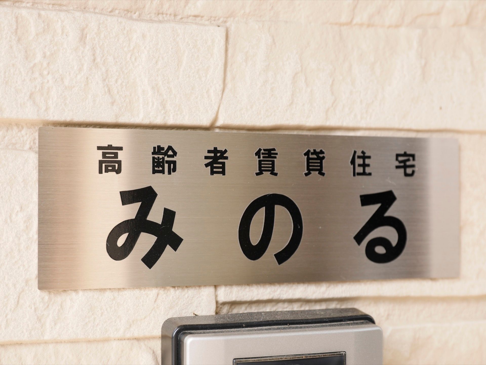 インターフォンの上に、銀色のプレートに黒い文字で施設名の描かれた表札がある。シンプルでわかりやすい設備である。