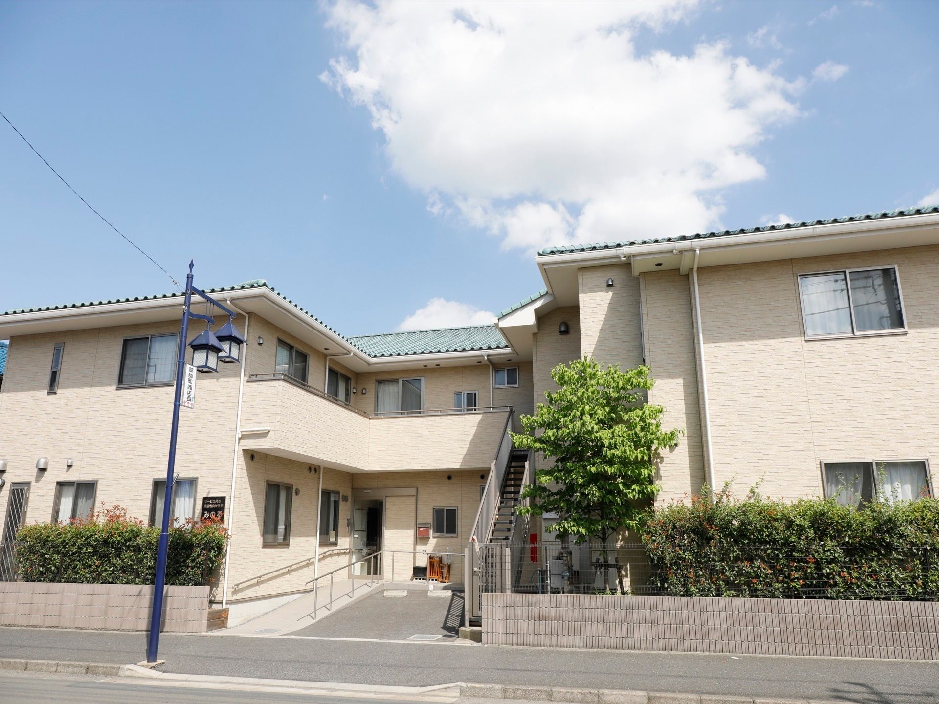 歩行者道路からは、スロープが伸びている。２階建てでグリーンがかった屋根が目印である。外階段もついている。