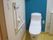 居室のトイレである。白を基調としたトイレに、背面の青い壁がアクセントになっている。便座の周りには手すりが取り付けられている。