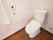 トイレは白い壁で清潔感がある。壁には手すりがあり、温水洗浄便座を採用している。床はダークブラウンで落ち着いた雰囲気である。