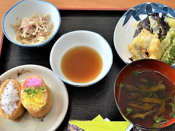 錦糸卵などの具材がのったいなり寿司やお吸い物、てんぷらなどが配膳されている。折り紙で作られた箸袋が置かれている。