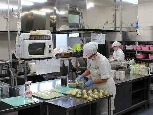 広々としたキッチンで食事をつくる、衛生帽をかぶったスタッフ