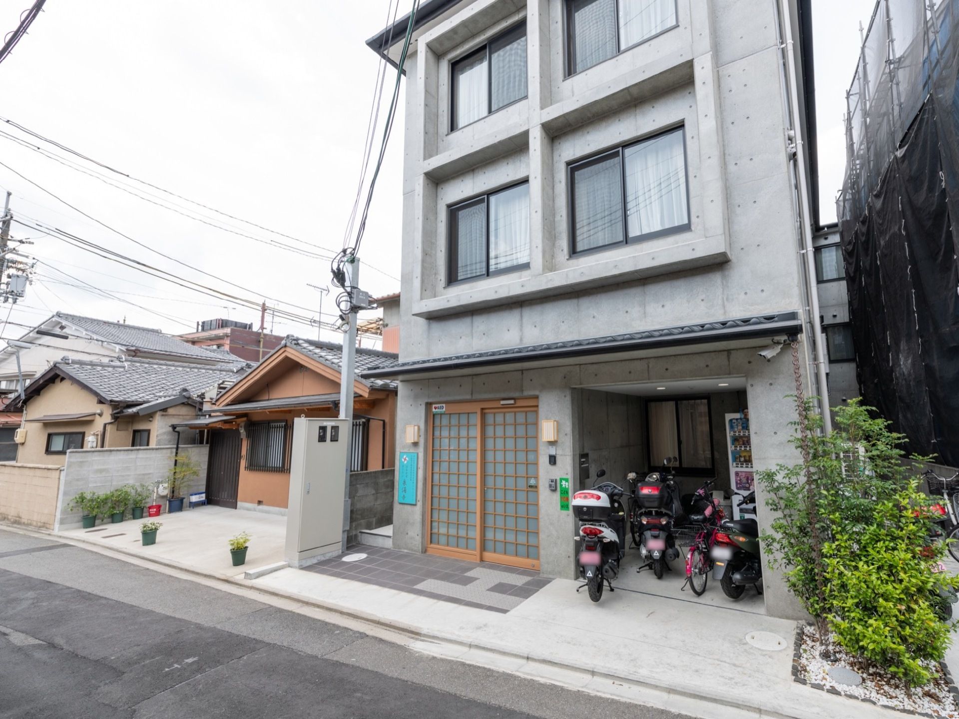 建物の前方には細い道路が通っていて、周囲には民家が建ち並んでいる。住宅街に溶け込む落ち着きある外観となっている。