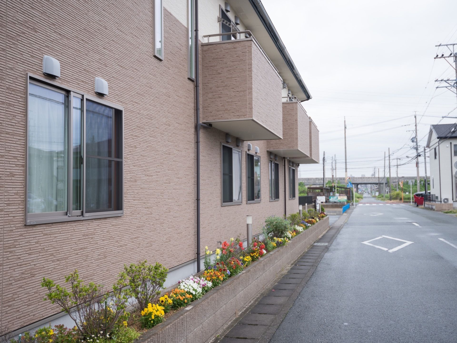 片側一車線の道路に面した2階建ての集合住宅がある。周囲には戸建てがあり、道路の先には鉄道の線路も見える。