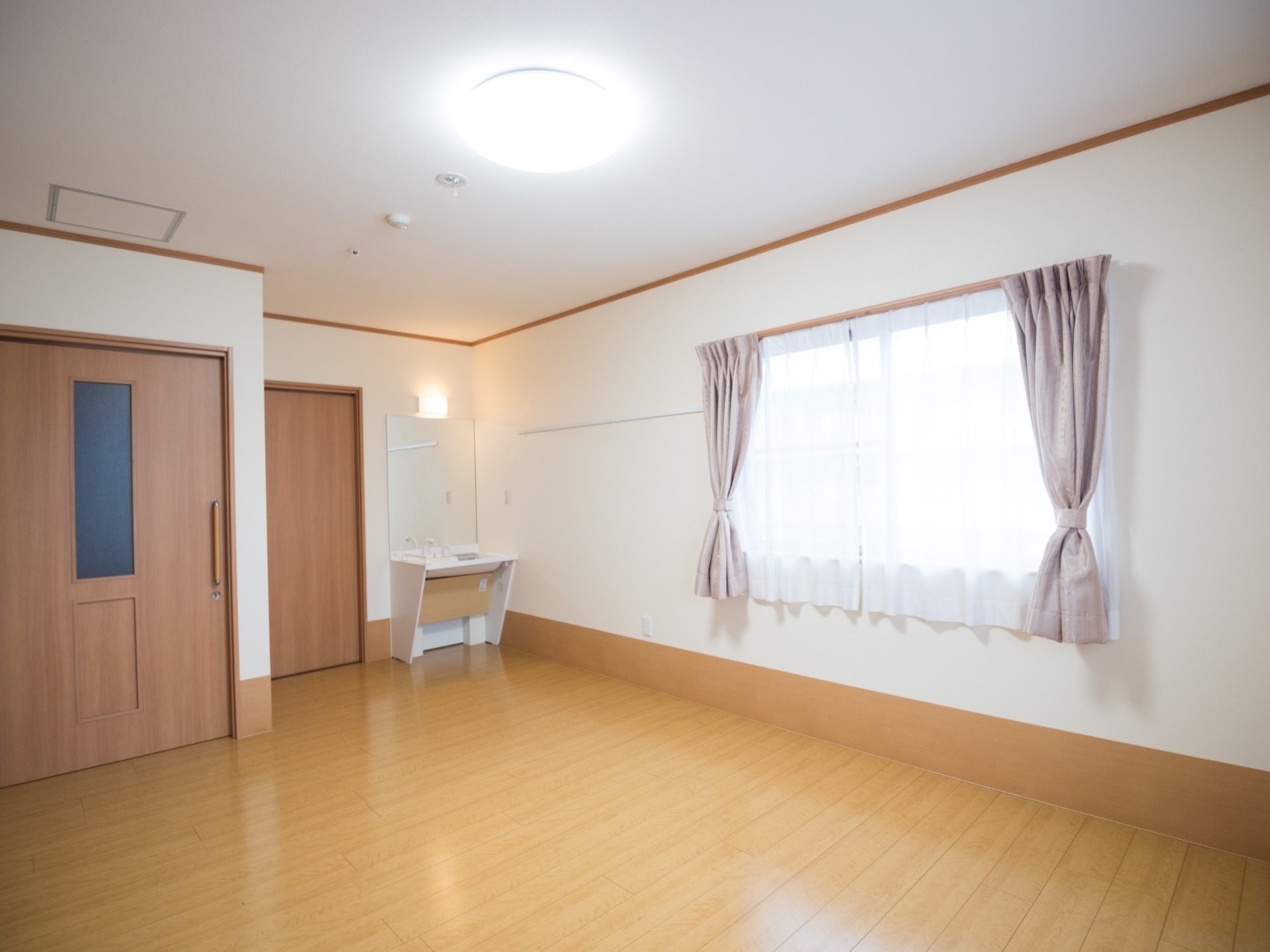 大きな引き戸のついた居室がある。床はフローリングになっていて、腰の高さに窓が設置されている。部屋の隅には鏡のついた洗面台がある。