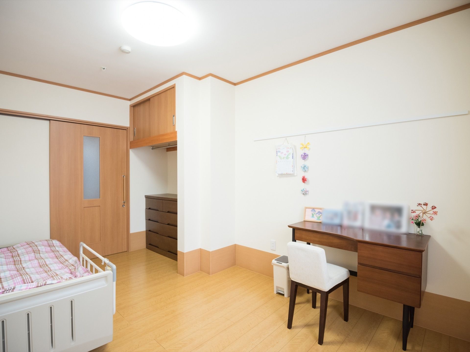 フローリングの部屋があり、入口の近くにベッドが置かれている。扉の横には木製のチェストやハンガー掛けのついた収納がある。