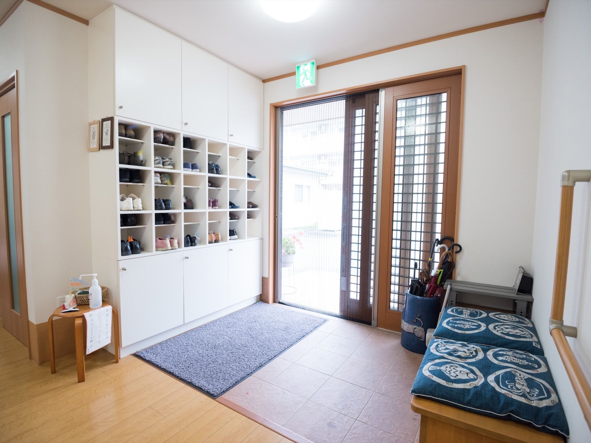 玄関は段差がなく、開け閉めしやすい引き戸になっている。下駄箱の反対側にはベンチがあり、座布団が置かれている。