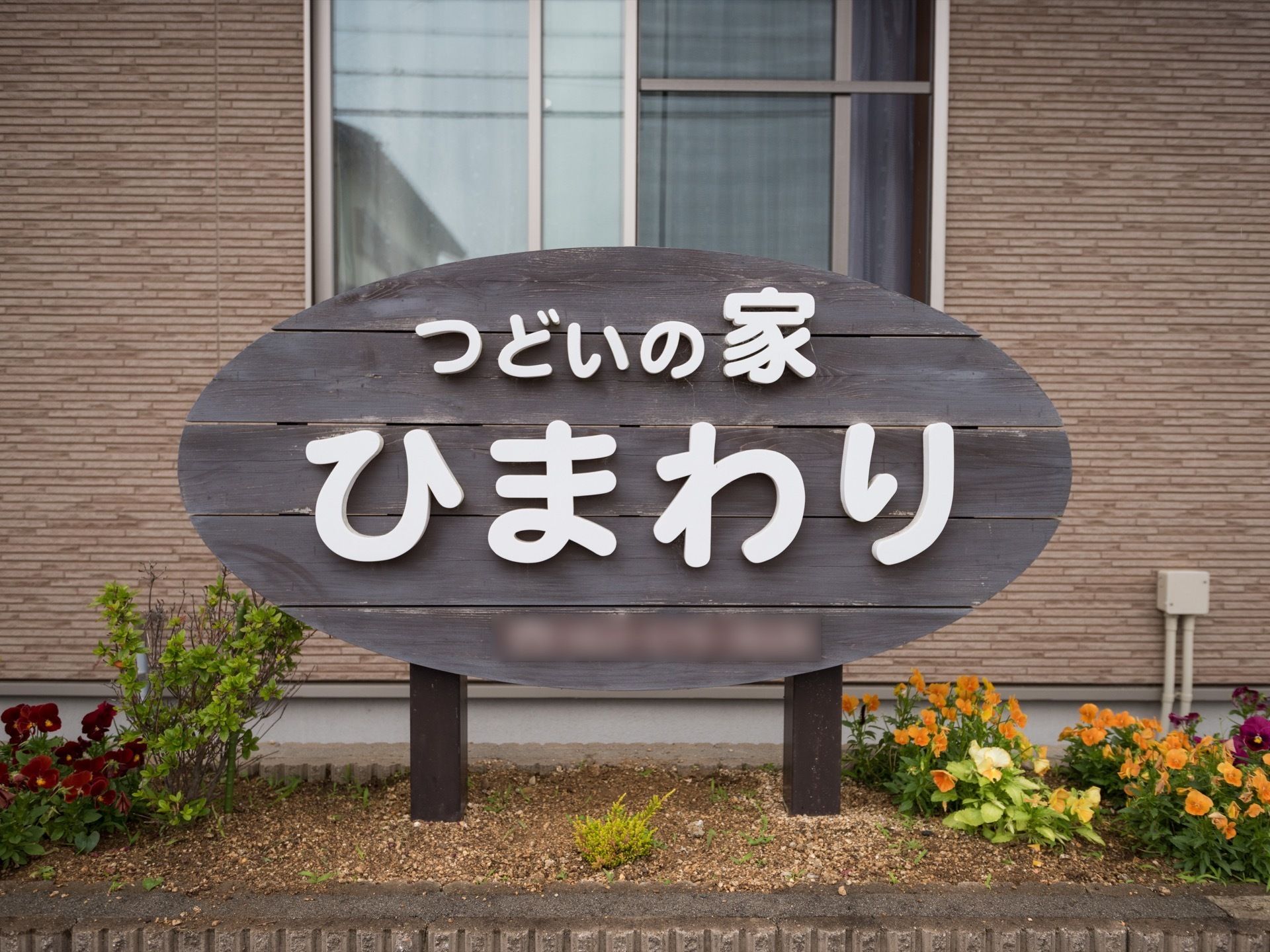 住宅の手前に花壇があり、そこに黒くペイントした木材と、白い文字板で作られたホームの看板が立てられている。