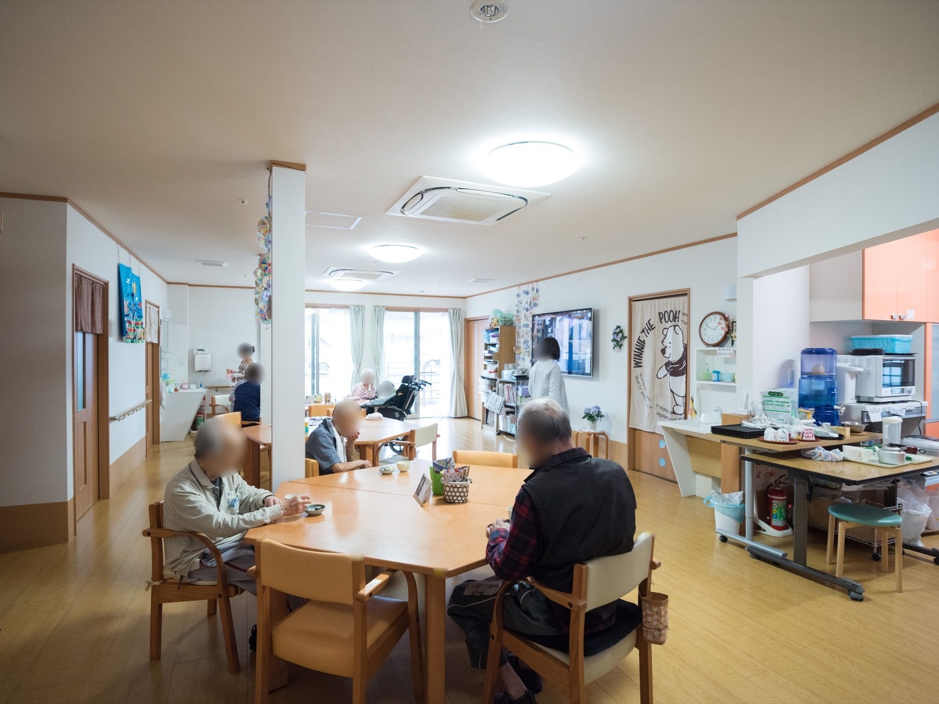 テーブルが並べられたフロアで、入居者様がお茶を飲んでくつろいだり、テレビを鑑賞したりして過ごしている。