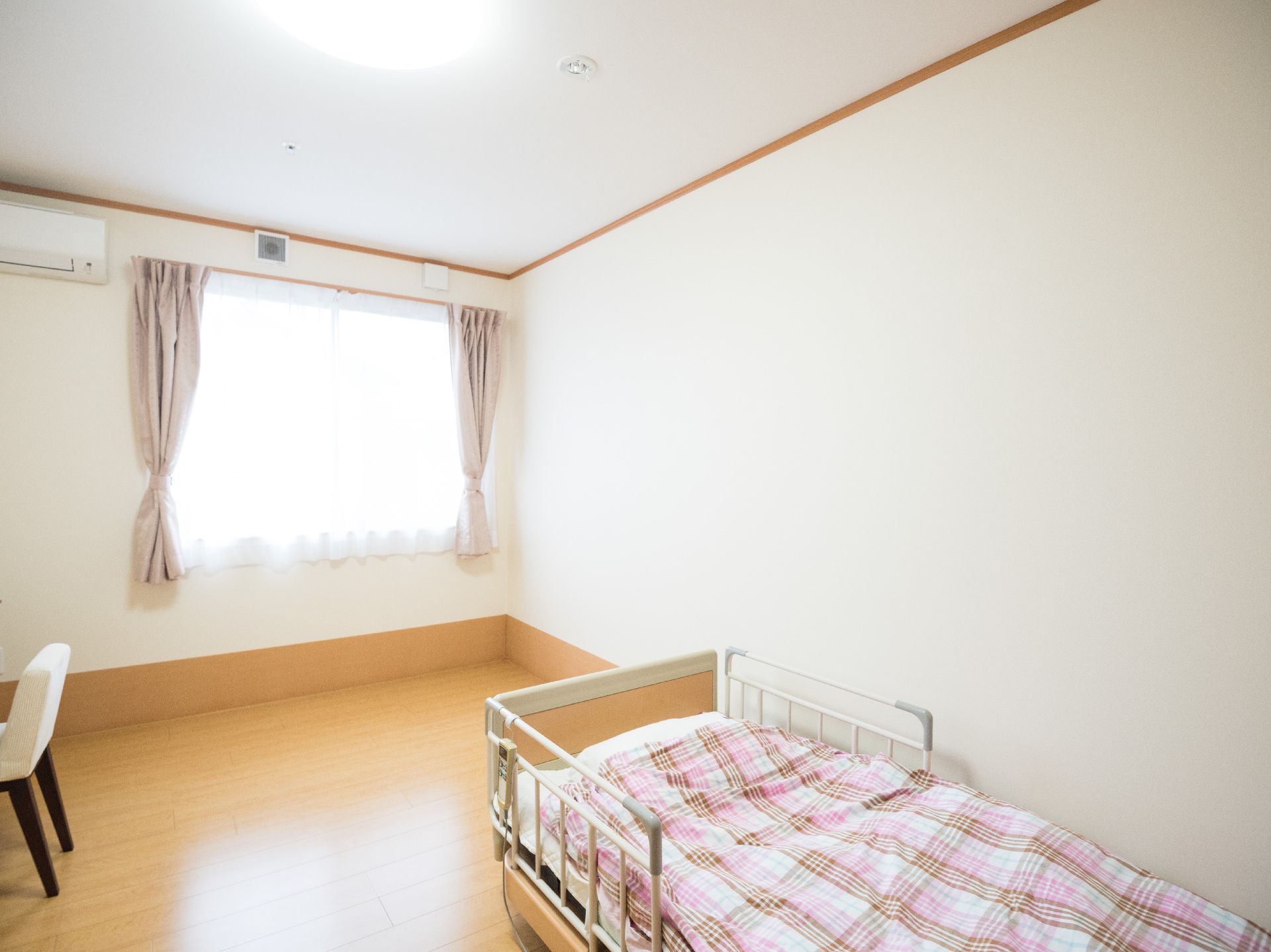 ピンク色のチェック柄の掛け布団がかけられた介護ベッドのある居室