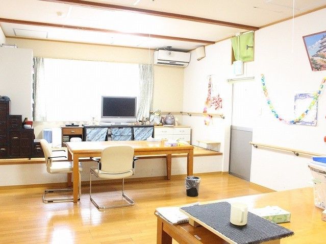 フローリングの床にテーブルと椅子が置いてある。小上がりになった所にこげ茶色の和風のタンスと小型の薄型テレビが置いてある。