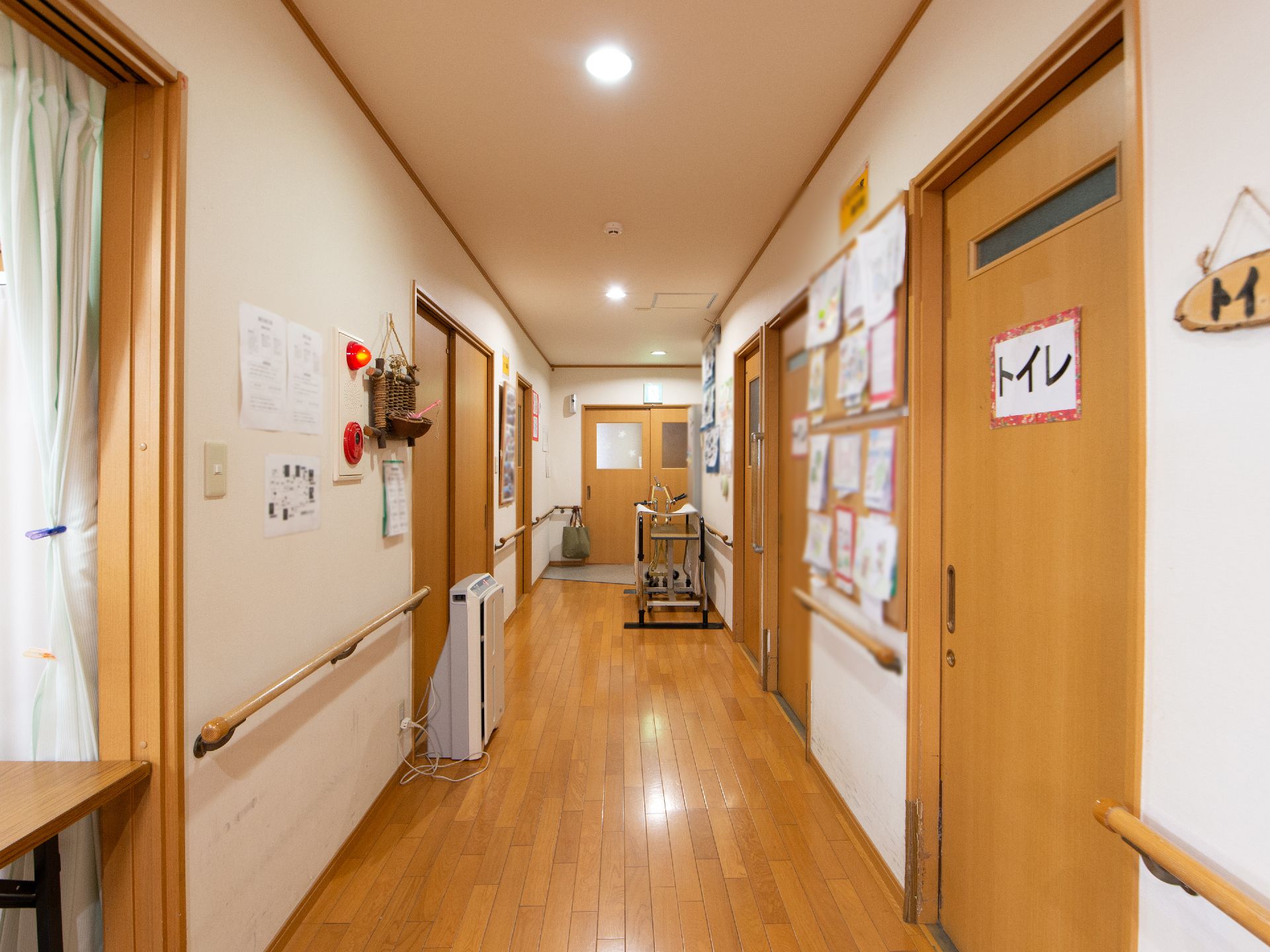 居室前の廊下はフローリング敷になっている。両サイドの壁には手すりが設置されている。廊下に歩行器が置かれている。