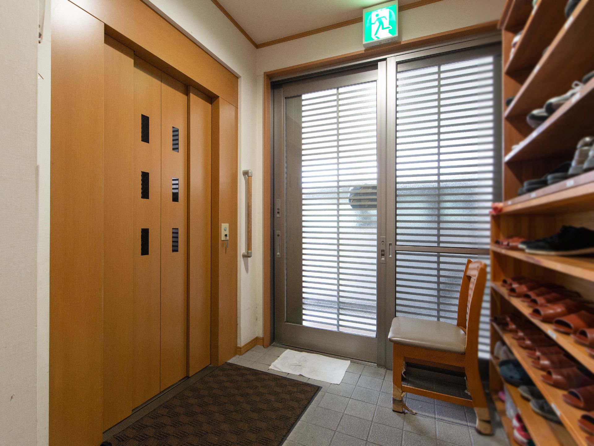 玄関の扉は広く開閉する木製になっている。木製の靴箱が設置されている。靴の着脱用の椅子が置かれている。