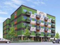 広い道路に面した５階建ての大きなグループホームである。２階以上の部分には、柵が取り付けられたベランダが設置されている。