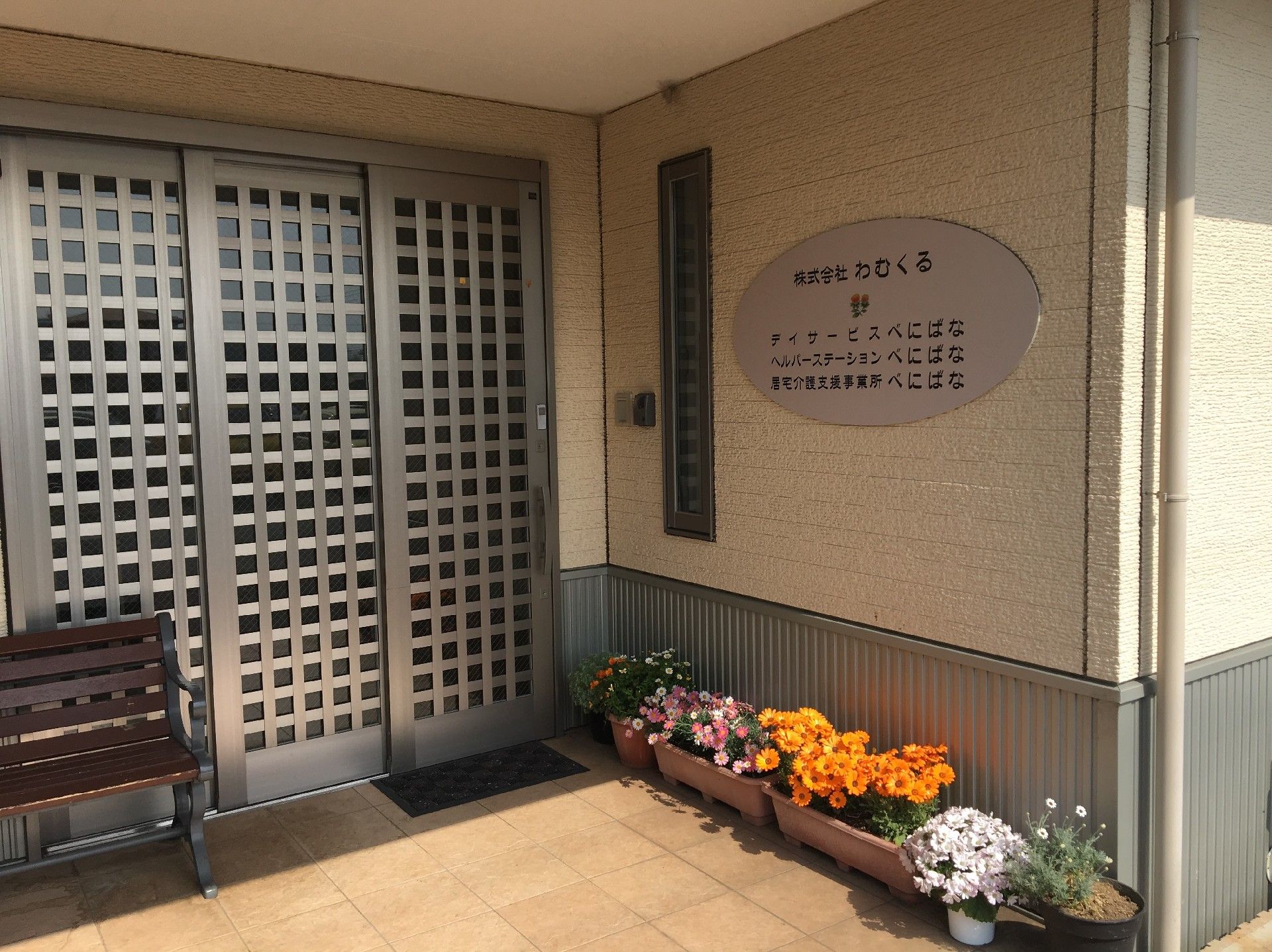 メタリックな格子の引き戸と傍にベンチが置いてある入口玄関