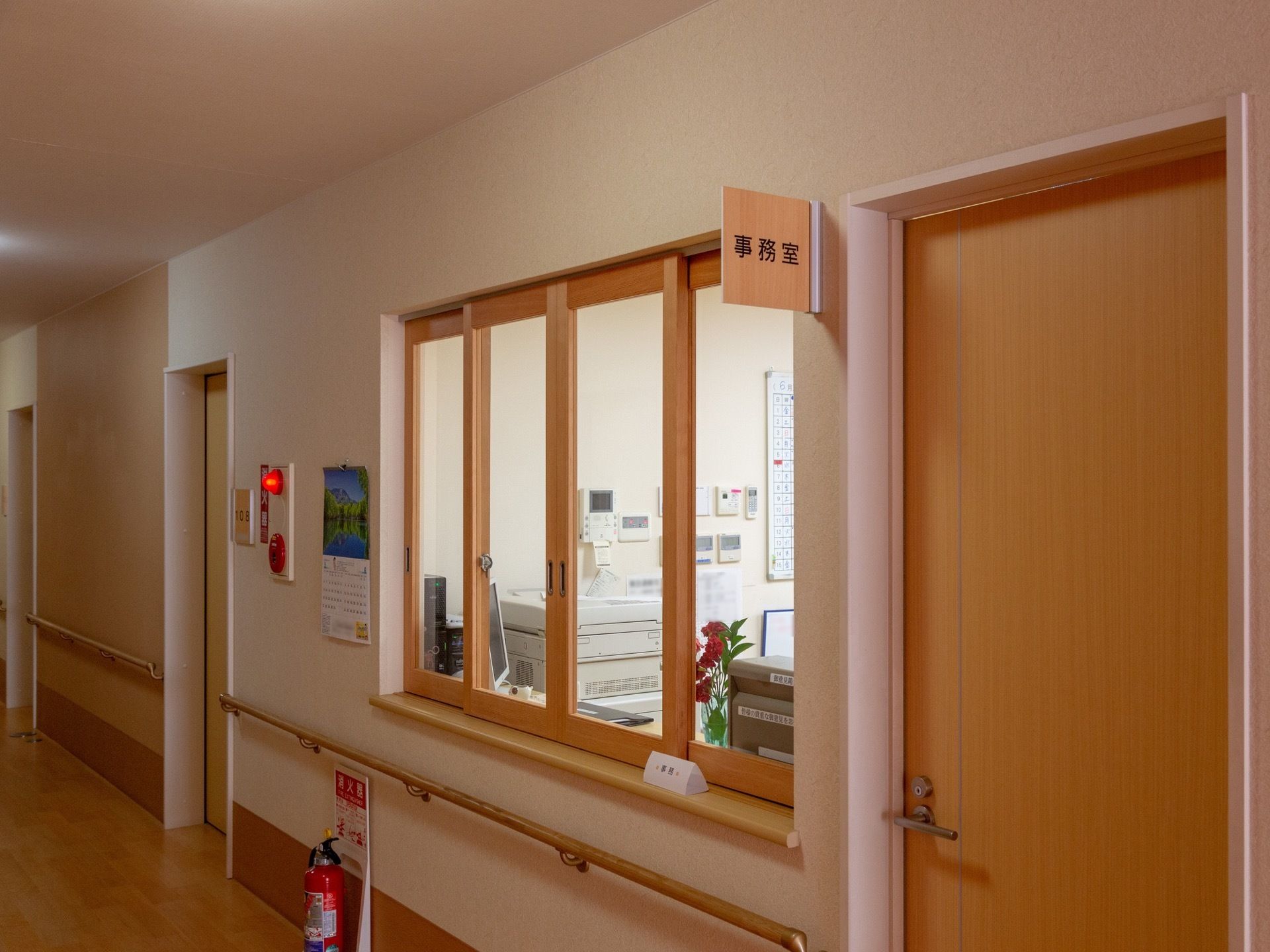事務室と書かれた木のプレートが掲げられている。入り口は木のドアとなっていて、その横にガラス窓がはめられ、窓口となっている。