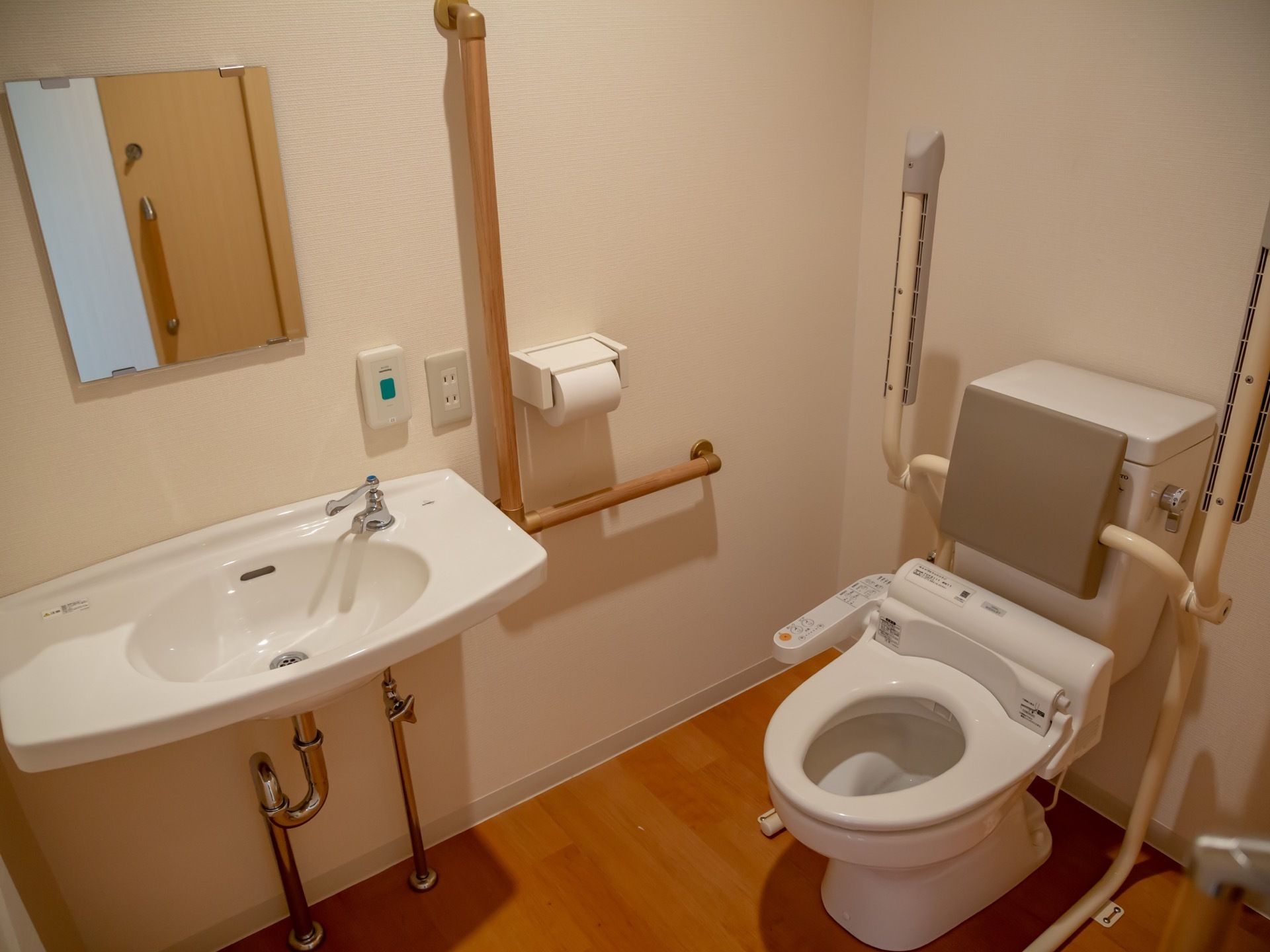 トイレには可動式の手すりと背もたれが付いているので安心して利用できる。また、同じスペースに洗面台も設置されている。