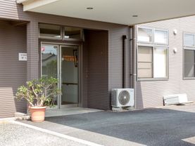 建物入口まで車を付けることができる。天井もあり、雨除け日除けになる。ベンチも用意されている。大きめの盆栽が飾られている。
