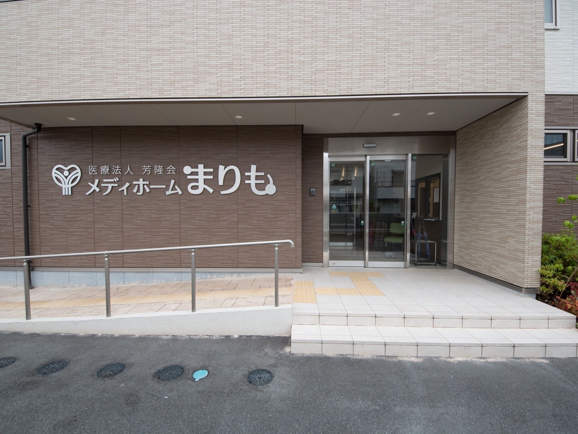 外壁の一部に大きく施設名が表示されている。手すりが取り付けられたスロープがある。玄関は自動ドアである。