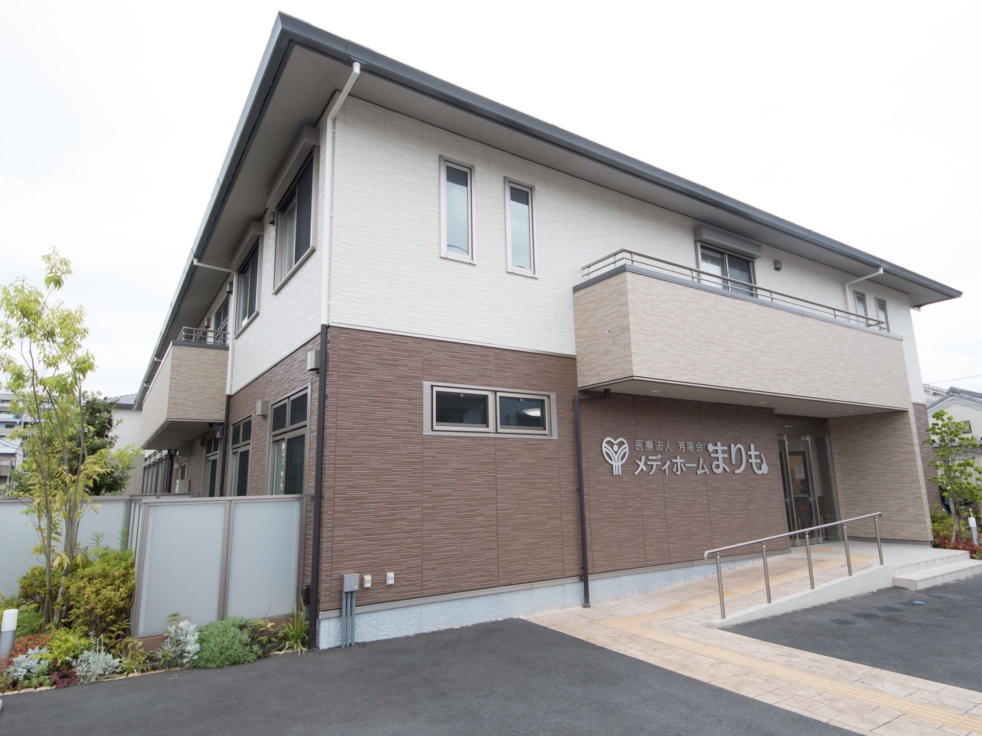 ２階建ての建物である。大きく表示された施設名が見える。敷地内の一部には植樹がされている。スロープがある。