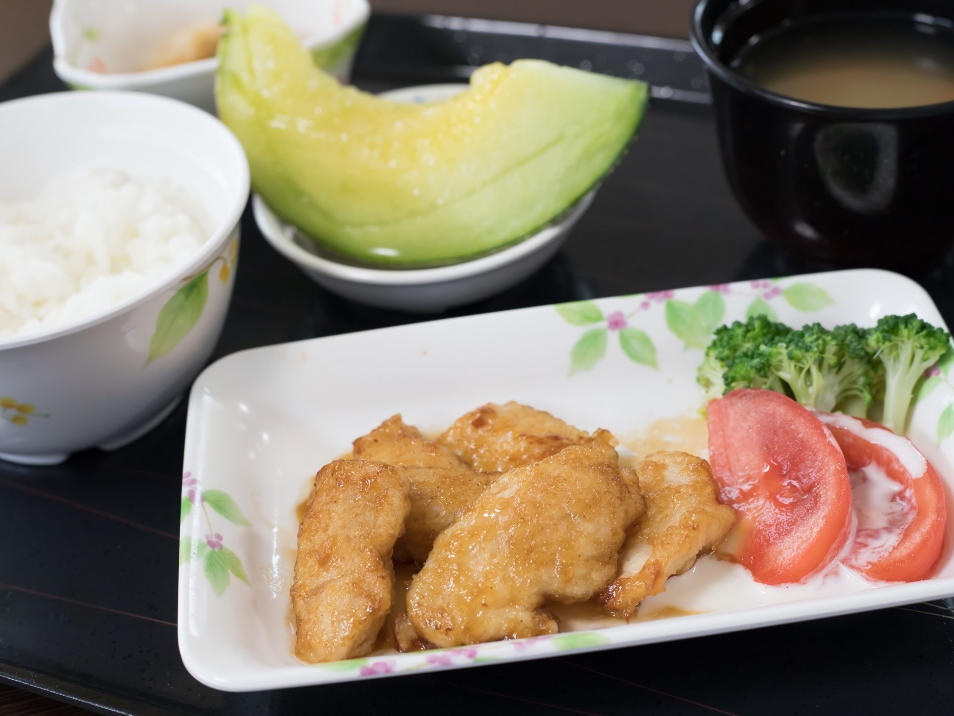 メインは鶏肉料理で、ドレッシングのかかった野菜が添えられている。米飯と汁物と果物が一緒に供されている。