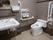 シックな色合いの壁紙のトイレに、洋式トイレと洗面台が設置されている。ナースコールや手すりが備わっている。
