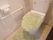 洋式トイレに、淡いグリーンのトイレカバーとマットが敷かれている。壁に白色のL字型の手すりが設置されている。
