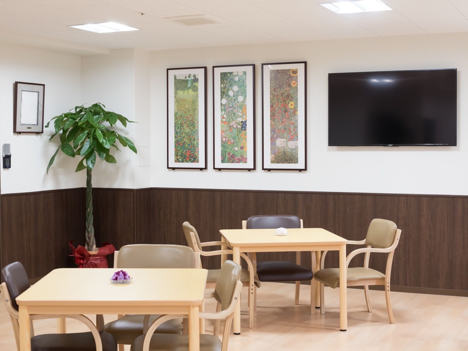 テレビの横に花をモチーフとした絵画が3枚飾られている食堂