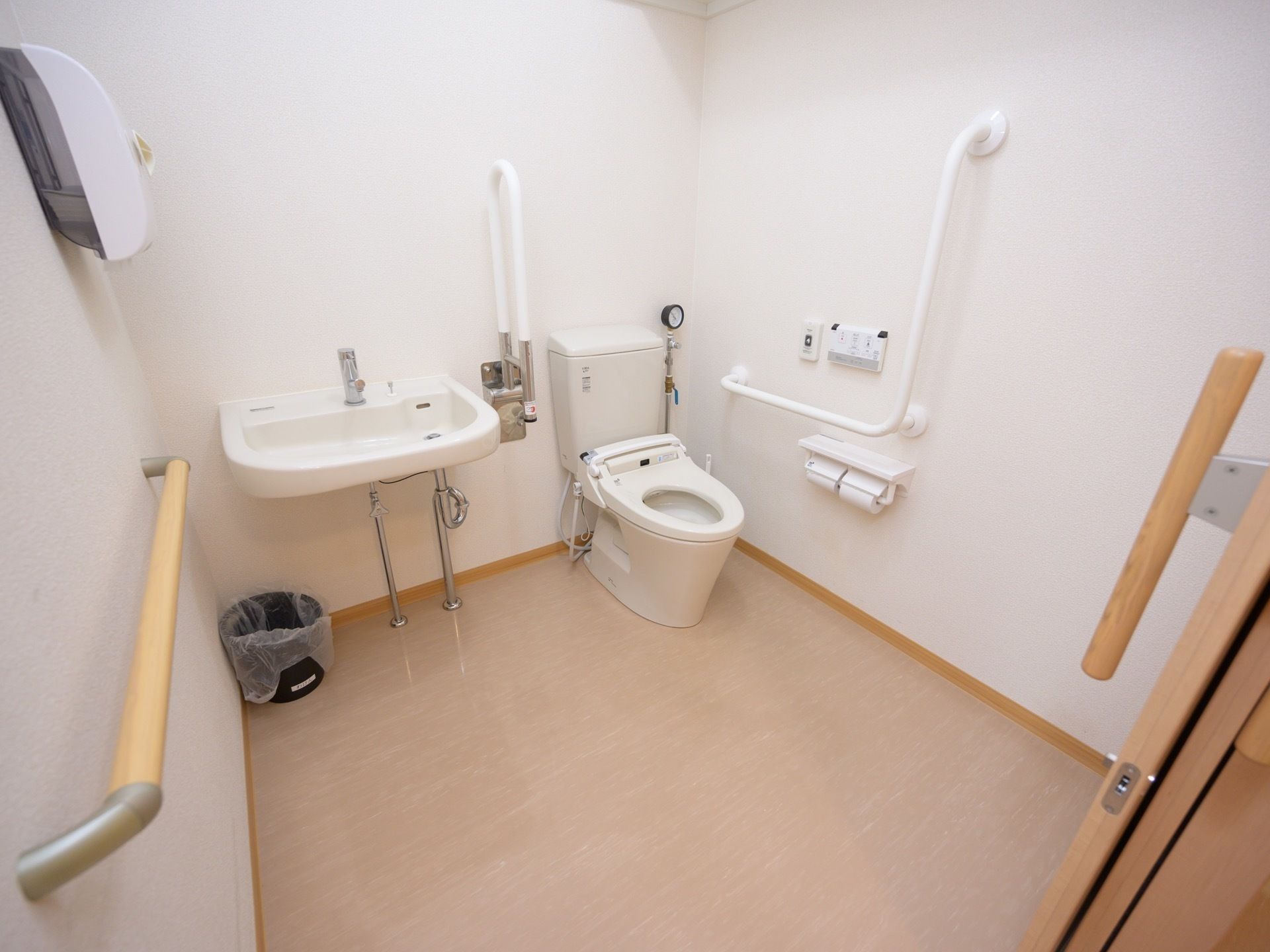 ゆったりとしたスペースが確保されたトイレの個室である。白色を基調とした清潔感のあるトイレで、便器と洗面台が併設されている。