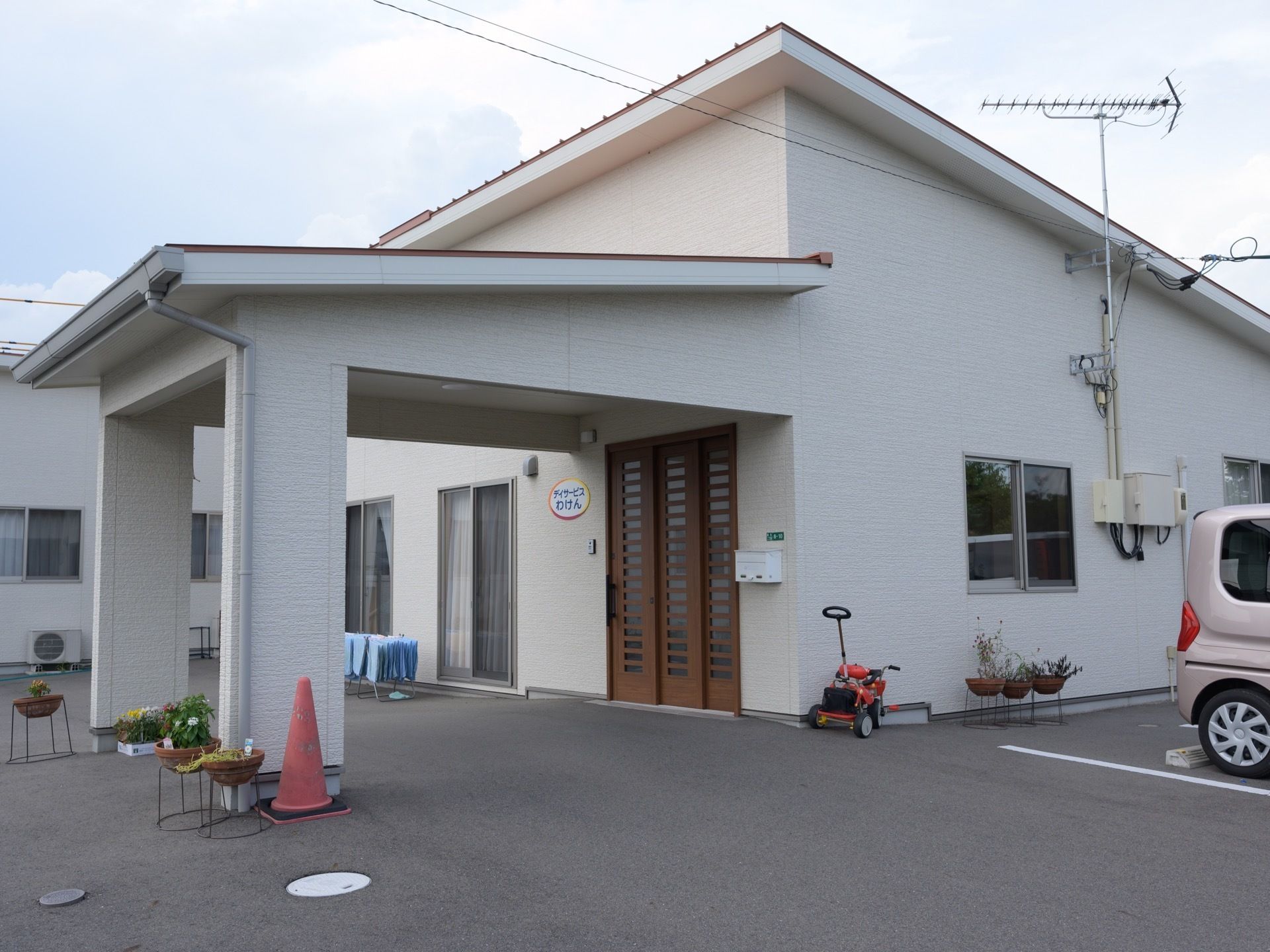 施設の建物は白色を基調とした洋風の外観である。玄関の茶色のドアの前にはひさしが設けられ、車を横付けすることができる程のスペースがある。