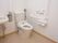 洋式のトイレの個室で洗面台が併設されている。便器の左右には手すりが備わり、一方は上下に可動するもので、もう片方は壁に備わるL字型である。
