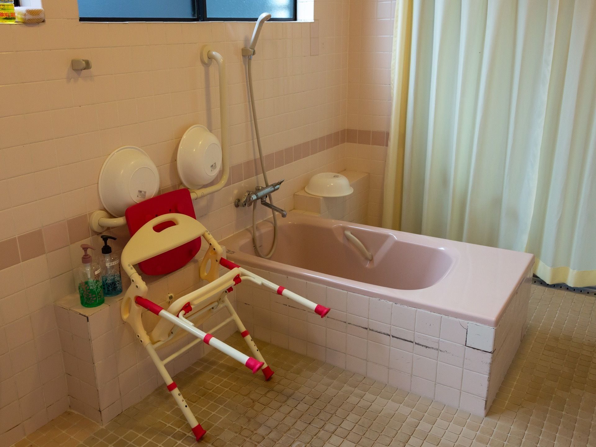 ピンク色の可愛らしい浴槽があり、床はタイル敷きになっている。台にはシャンプー類が並んでおり椅子もある。