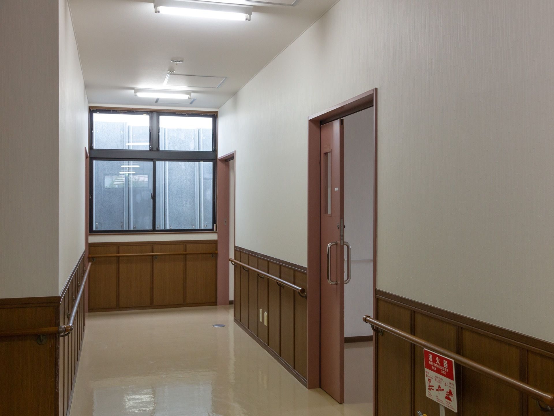 施設内の廊下には、つかまりやすい高さのところに茶色い手すりが設置されている。ドアはスライドタイプである。