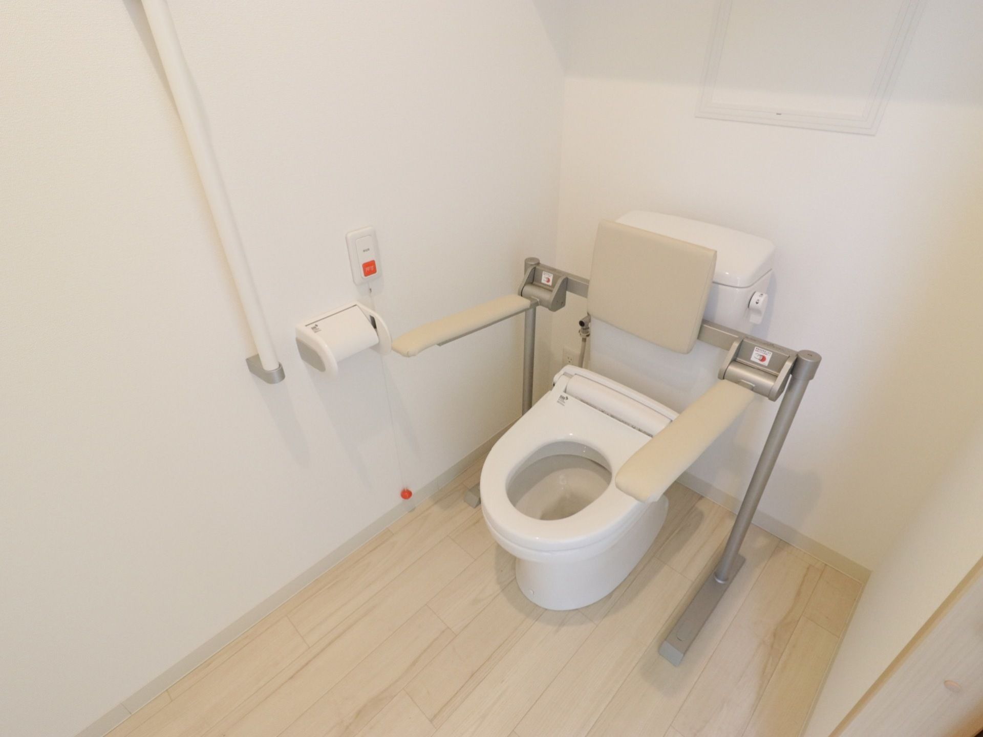 トイレの便器には、背もたれが付いた跳ね上げ式ひじ掛けが設置されている。呼出ボタンとI型手すりが壁に備え付けられている。