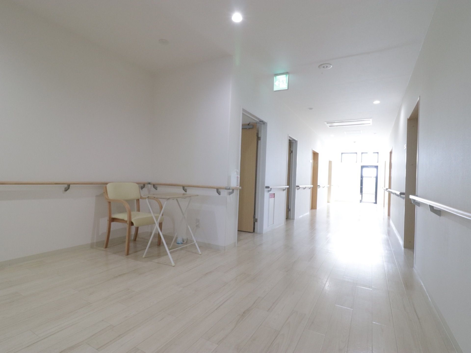 明るく広い廊下である。左右の壁に沿って手すりが取り付けられている。壁際にテーブルと椅子が置かれている。