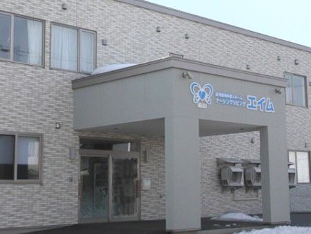 施設の玄関付近の様子である。玄関前の屋根付きの門には、施設名が表示されており、建物は２階建てである。