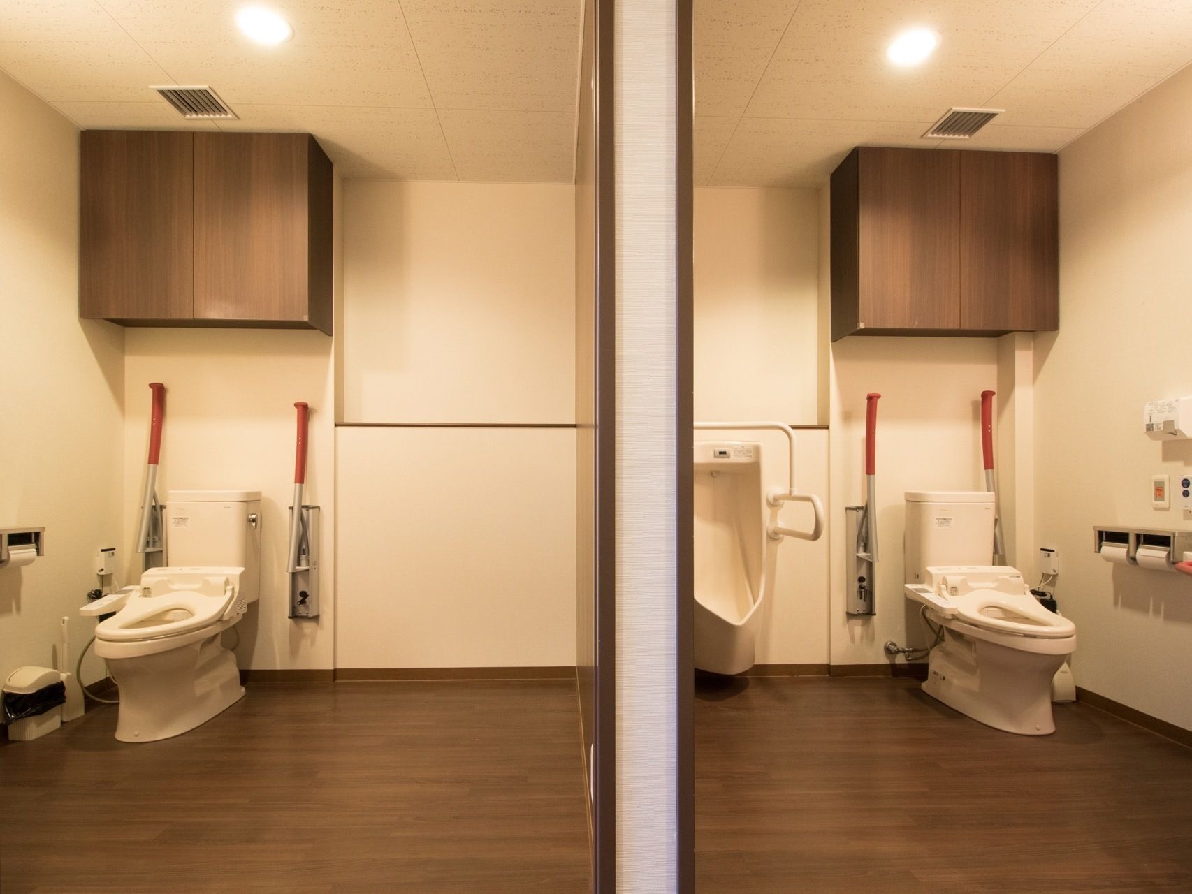 落ち着いた照明の広い個室トイレが２つあり、洋式便器が左右対称に配置されている。可動式のひじ掛けがついている。片方には男性用便器もある。