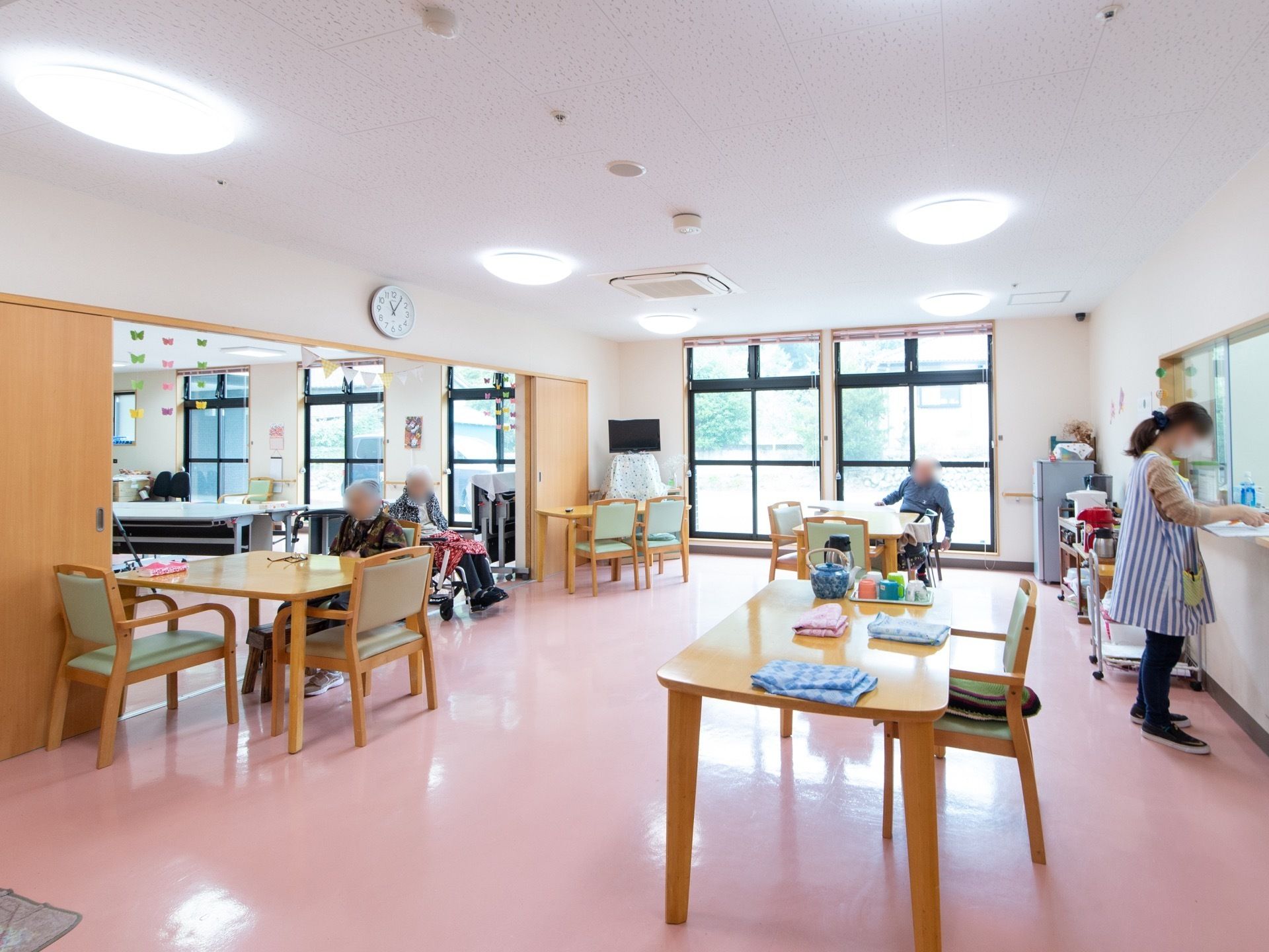 窓が多く、たっぷりの日が差し込む。テーブルや椅子がゆとりをもって配置されている。テレビが置かれている。