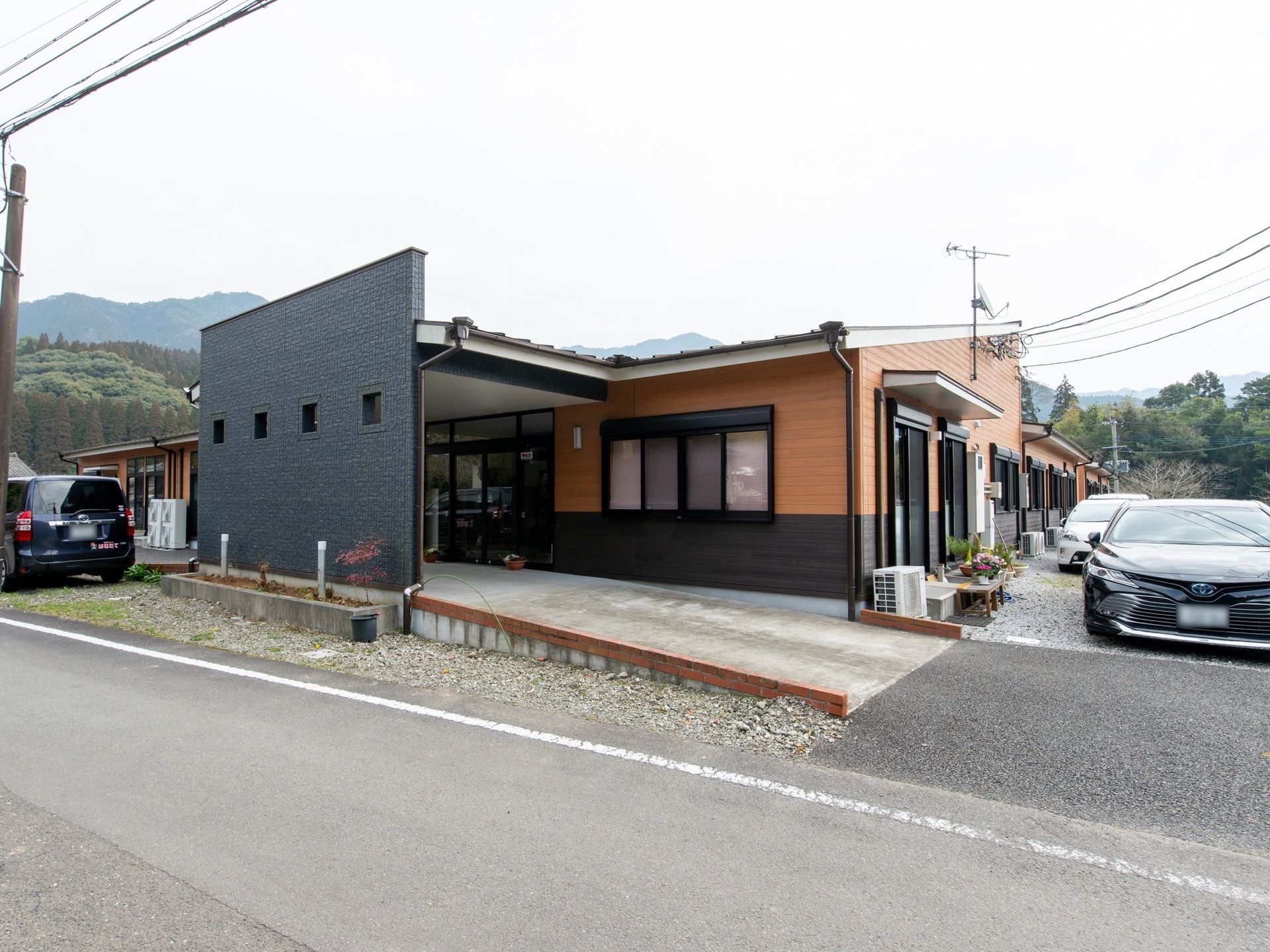 玄関には大きな屋根がついている。広々としたスロープになっている。駐車スペースが建物の脇に用意されている。