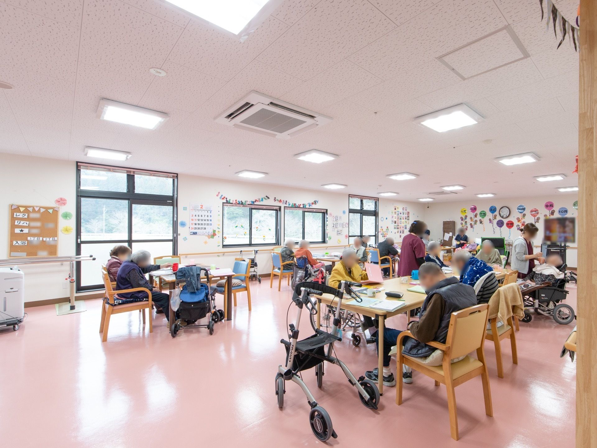 食堂には窓があり、明るく広々としている。入居者様が大勢席についていて、何か作業をしている様子である。