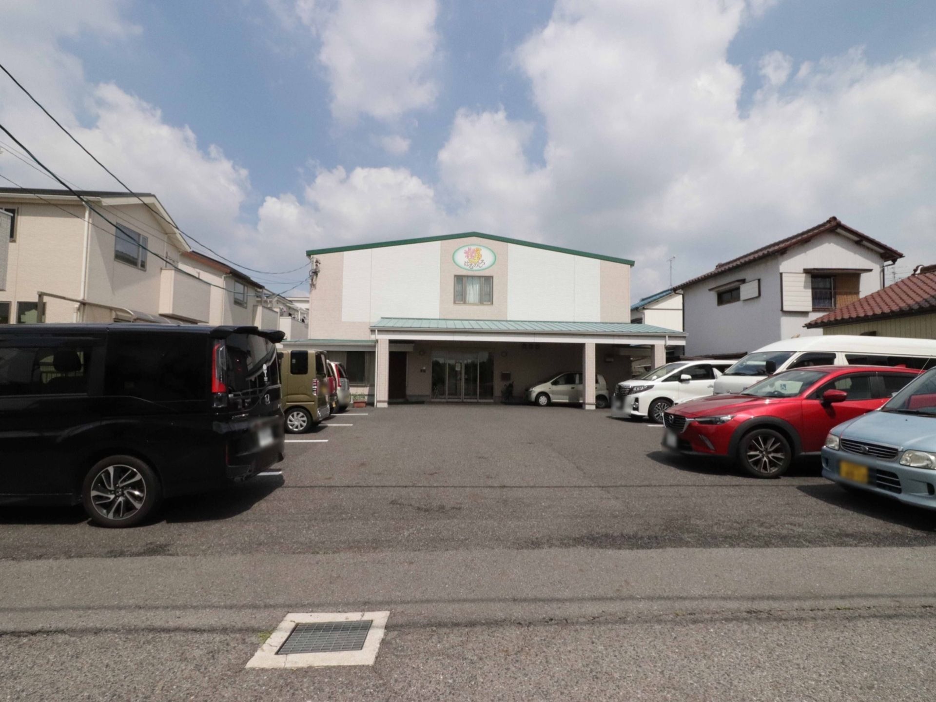 当施設の正面玄関の様子。建物上部には施設名とロゴマークが施されている。施設前には駐車場が用意されている。