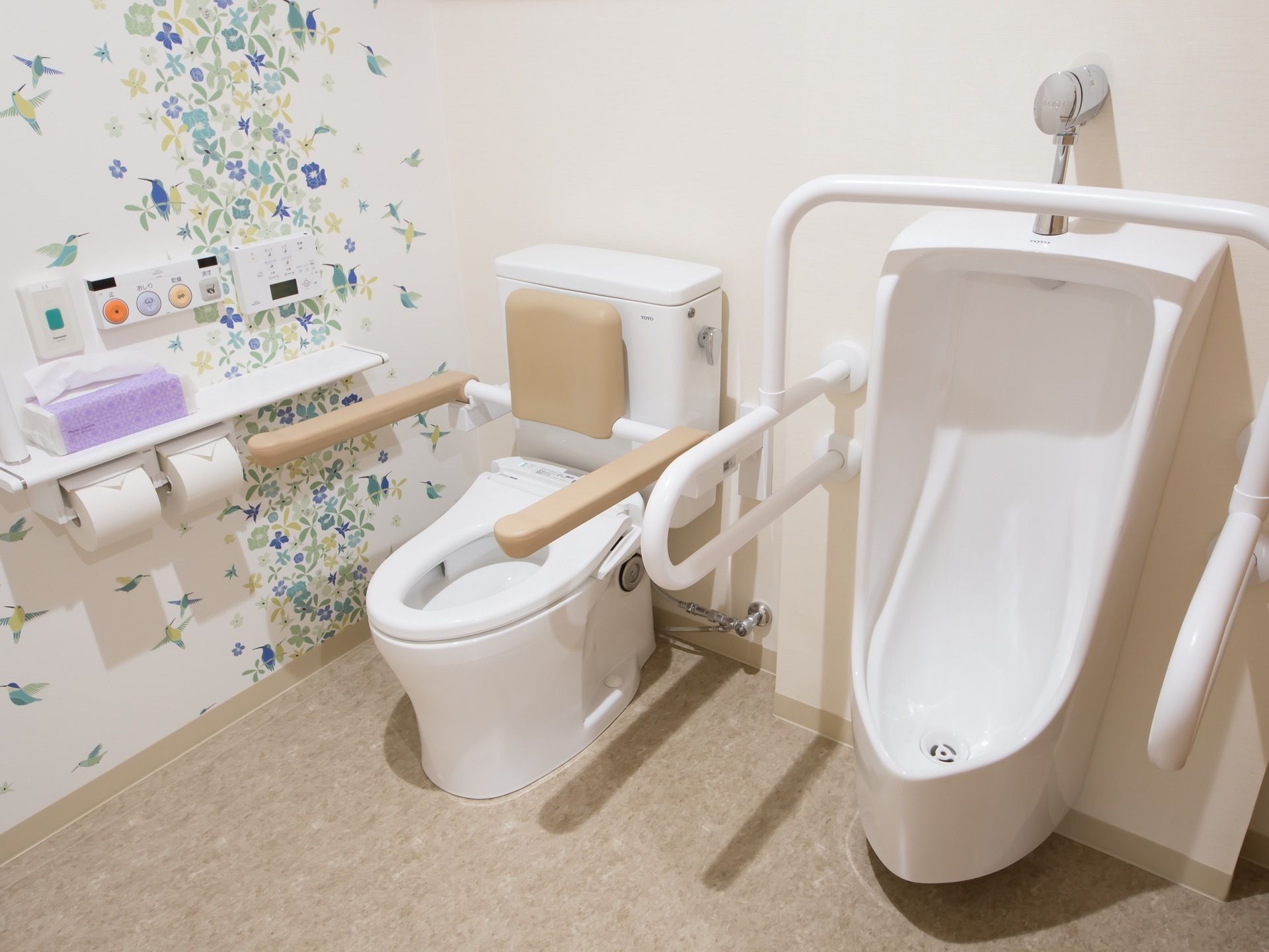 広いトイレの壁には、鳥や花のウォールステッカーが貼られている。男性用小便器と洋式便器が並んで設置されている。