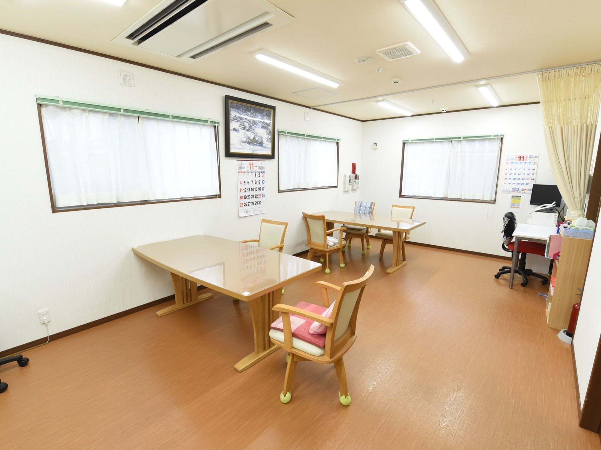 顔の高さあたりに設置された、複数の窓がある。窓には、白いカーテンがついている。窓の近くにテーブルセットが置いてある。