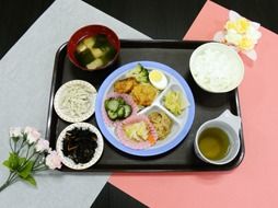 四角い紅白の敷きものの上に黒いお盆があり、その上に６品の食事が乗せられている。彩りが豊かで楽しい気分になる。