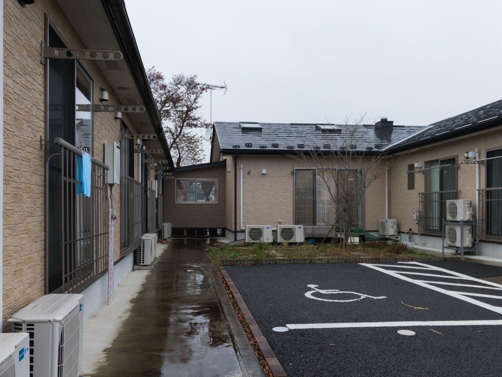 施設の中庭部分に駐車場が設けられている。各自の居室には窓とフェンス、洗濯物を干せる竿などが設置されている。