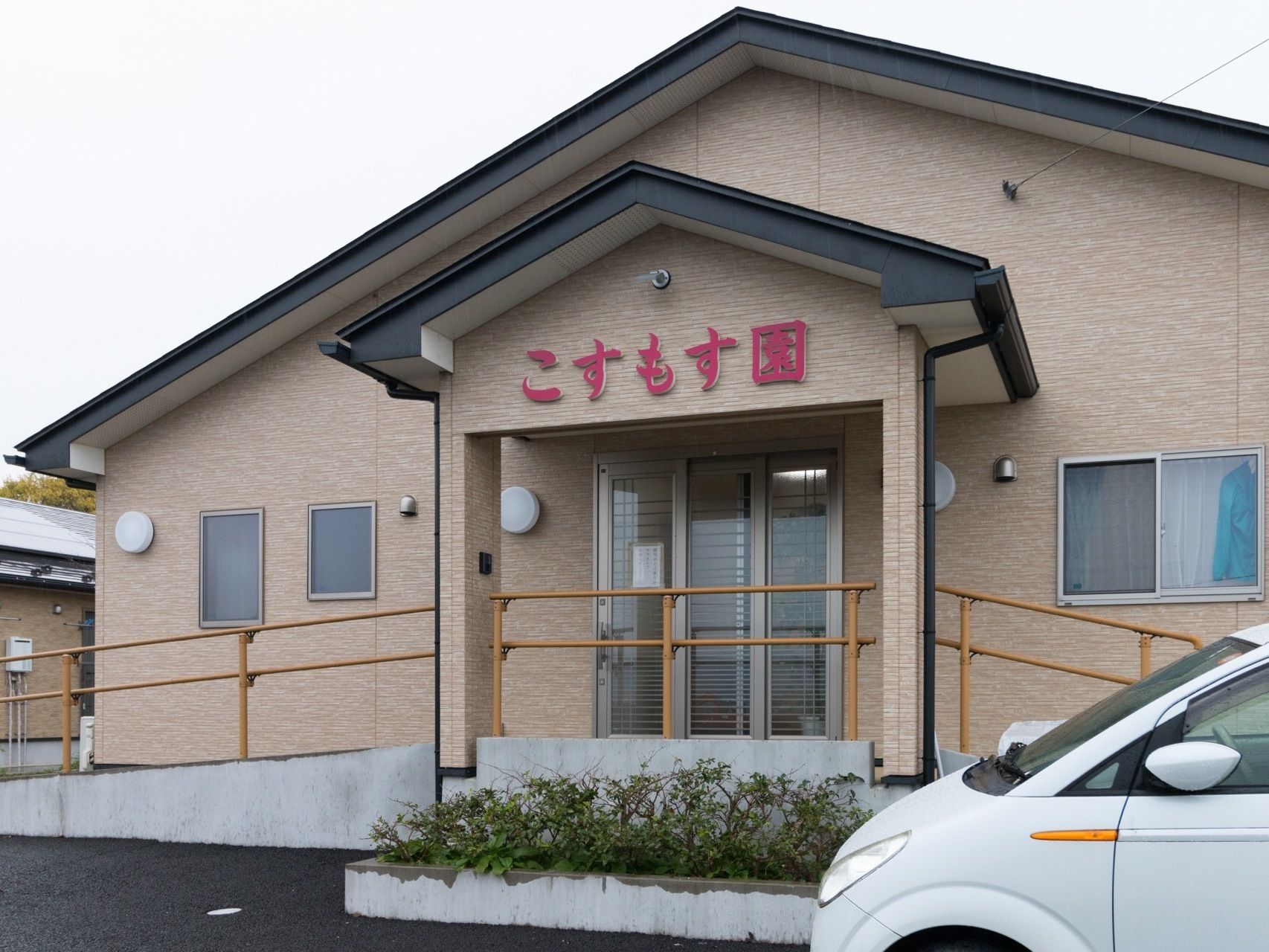 外玄関入口の様子である。屋根部分に赤い字で分かりやすく施設名が入っている。玄関前には2方向から利用できる手すり付きスロープがある。