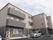 三階建ての建物が見える。一階部分と二、三階のベランダが同じ色である。その他の部分はベージュ色になっている。