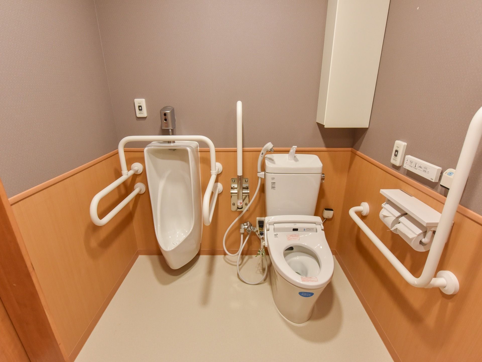 広いスペースがあり、小便器のまわりや壁には手すりが取り付けられている。壁の下半分は木目調になっており、上半分はグレーの色になっている。