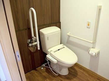 床面はブラウンのフローリングで段差がない。緊急通報装置、洋式便器が設置されており、壁面には手すりが付いている。