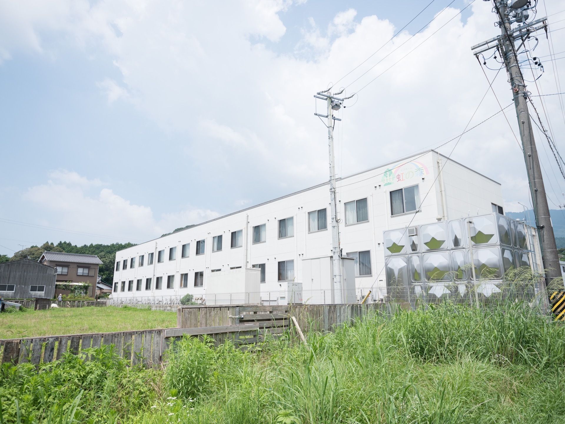 大規模で真っ白な２階建ての建物の施設。周辺は緑に囲まれた自然豊かな立地である。民家が数軒建っている。